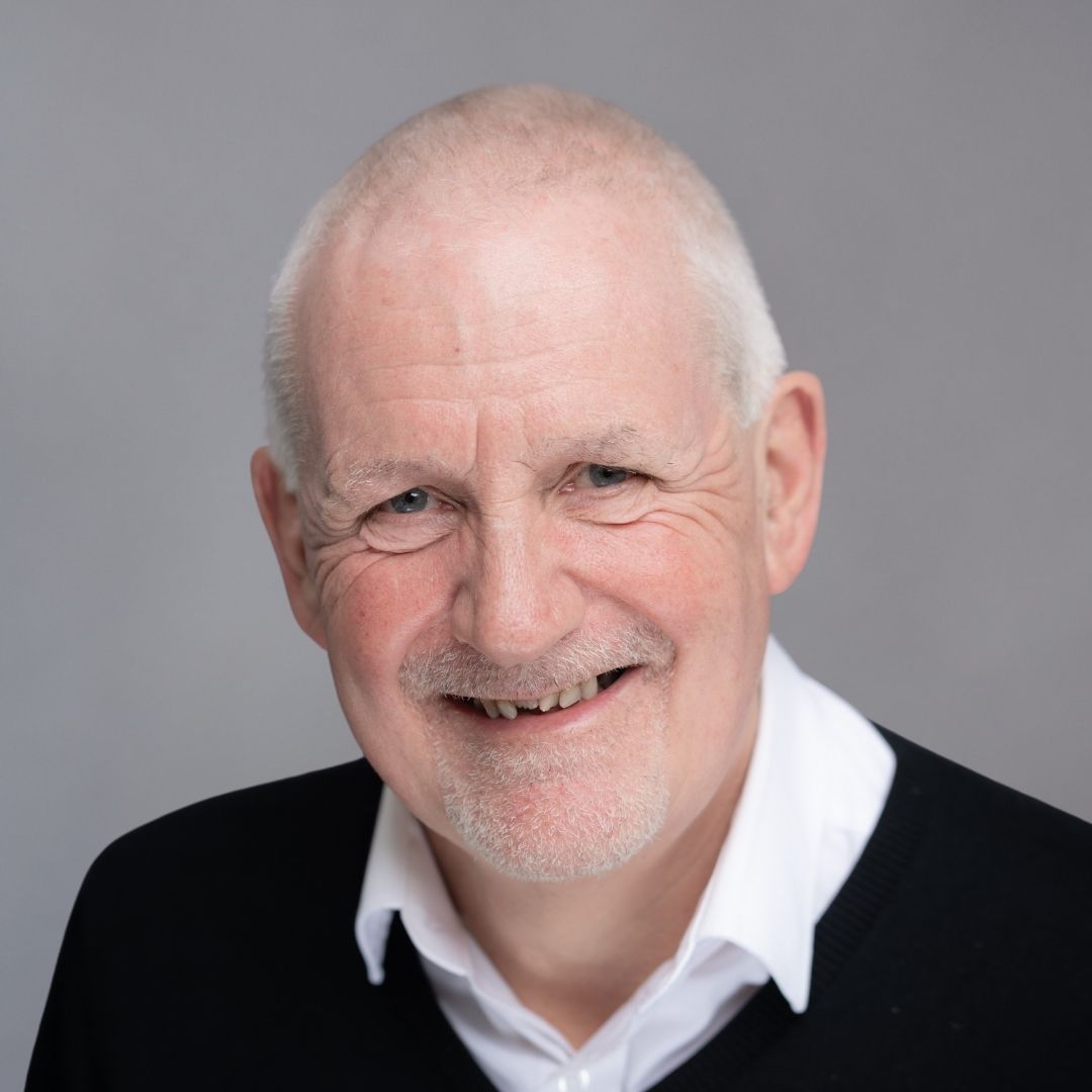 A smiling man wearing a white collared shirt and black blazer over it